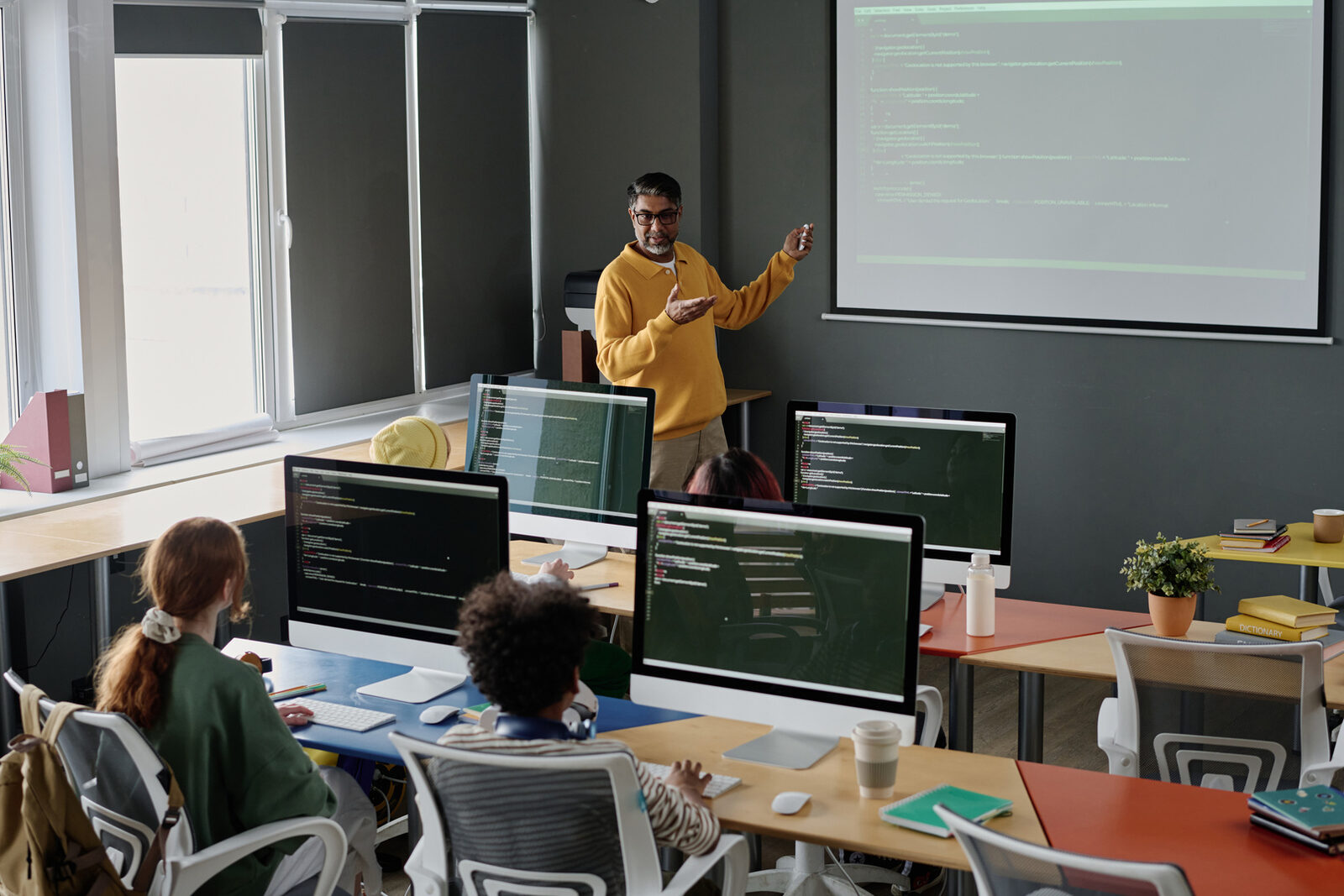 A teacher leading a coding class with students at computers