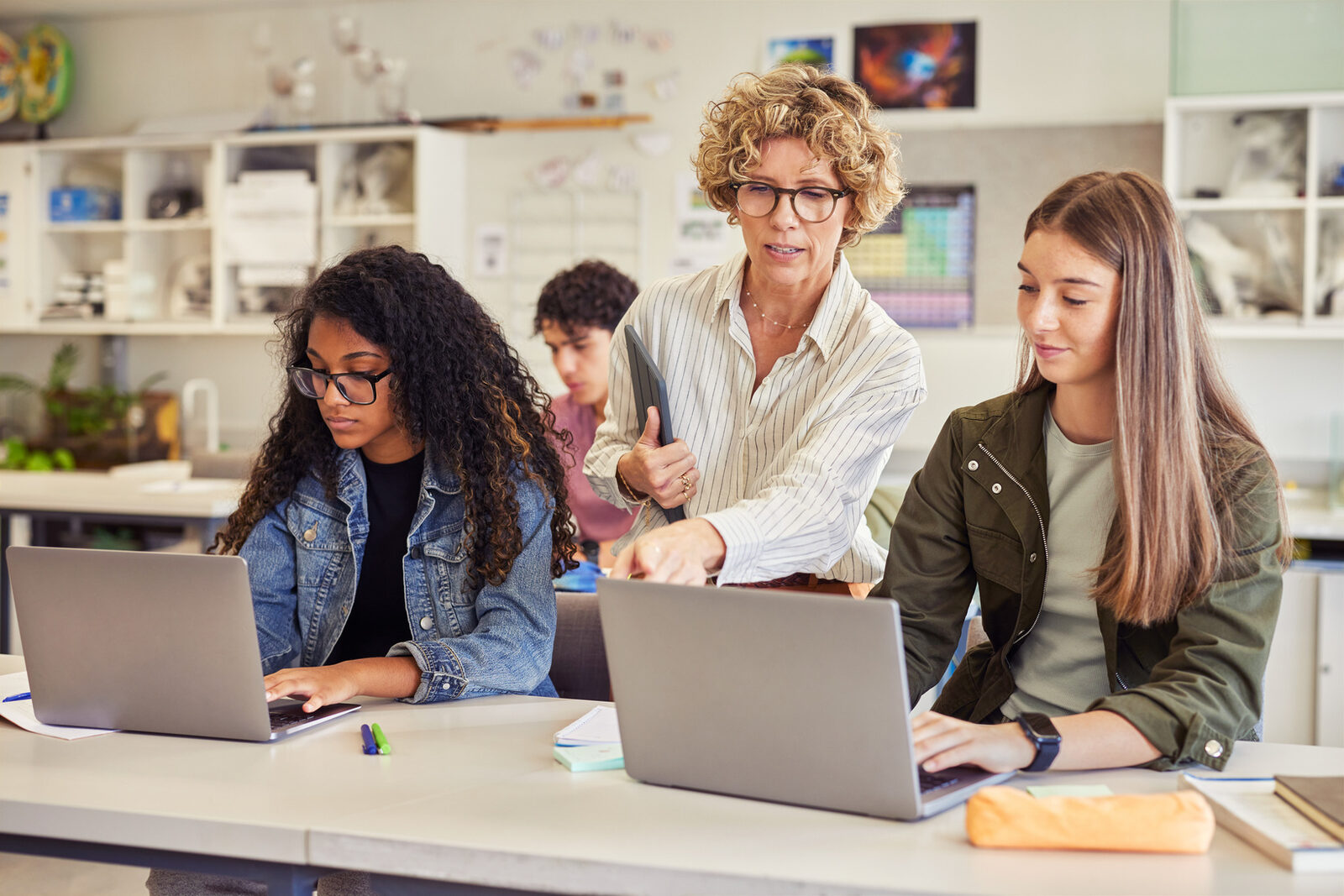 A teacher helping two students using laptops