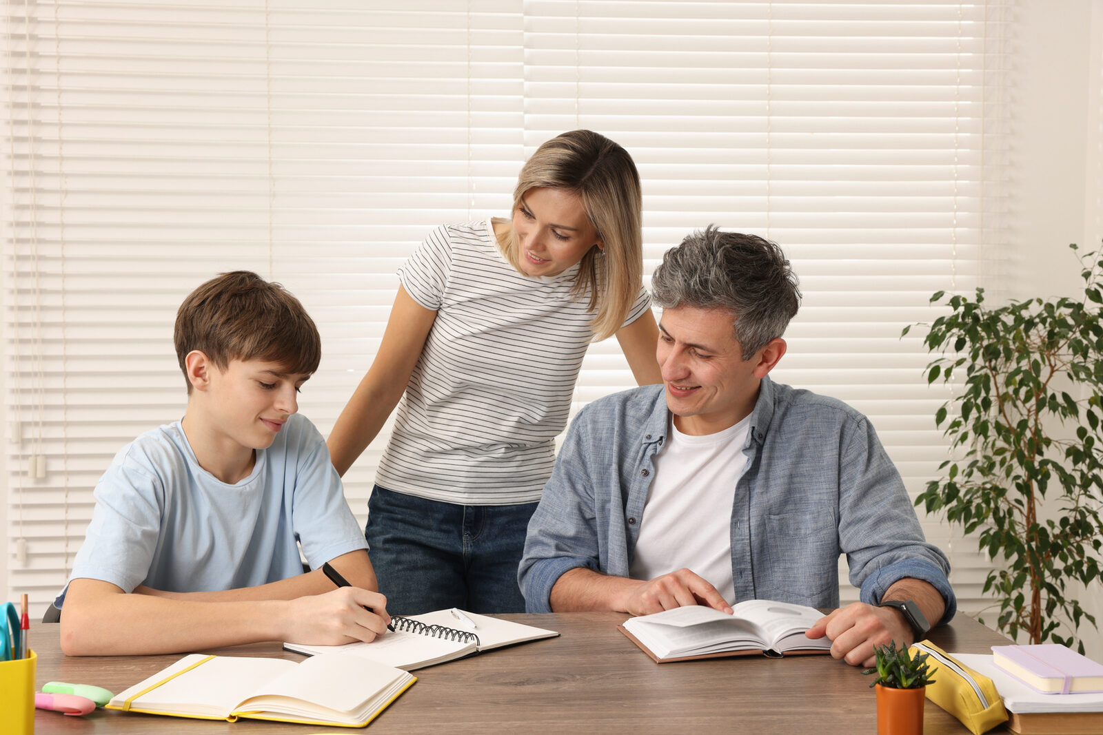 A teenager doing homework with parents helping at a kitchen table
